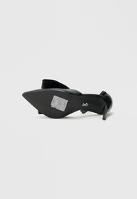 Schwarzer Pumps mit spitzer Zehe, glattem Material und dünnem Absatz. Verfügt über eine strukturierte Sohle mit einem weißen Barcode-Detail.