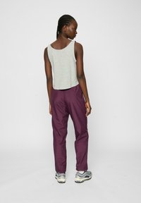 Sivi crop top bez rukava u kombinaciji s opuštenim ljubičastim hlačama, koje imaju glatku teksturu. Model nosi sportske tenisice s valovitim prugama.