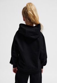 Svart huvtr öja i mjukt tyg, med avslappnad passform, ribbade muddar och en känguruficka. Minimalistisk design utan synliga logotyper.