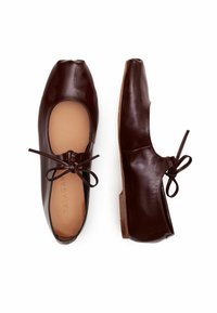 Bailarinas de cuero marrón oscuro con punta redondeada, un delicado lazo como acento y un tacón bajo; textura suave y detalles de costura mínimos.
