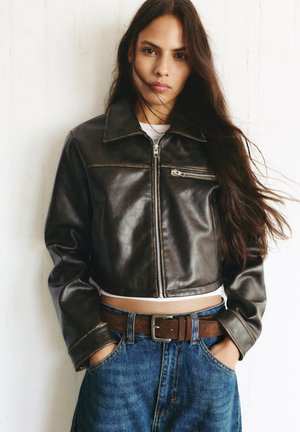 Brun læder cropped jakke med en frontlynlås, lige krave og kontrasterende syer, parret med en denim nederdel og bælte.
