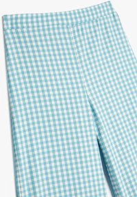 Niebieskie i białe spodnie w kratkę w stylu gingham o prostym kroju leżą płasko na białym tle.