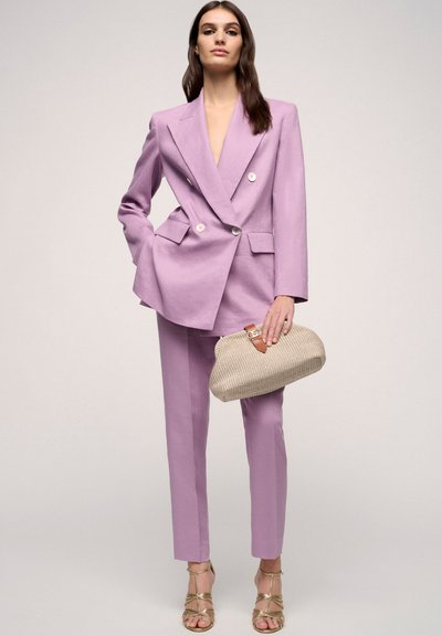 Lavender double-breasted blazer and matching tailored pants, paired with a textured beige clutch and strappy gold heels.