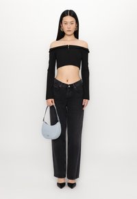 Čierny crop top bez ramienok s dlhými rukávmi, čierne nohavice s vysokým pásom a svetlomodrá kabelka, doplnené o čierne lodičky na vysokom podpätku.