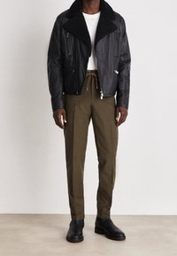 Svart läderjacka med en pälskrage, med dragkedjefickor, ihop med olivgröna byxor och svarta ankelstövlar. Slät textur, figursydd design.