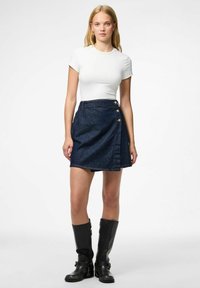 Denim wrap skirt with a dark blue wash, featuring three gold buttons on the side. Paired with a fitted white t-shirt and black knee-high boots.