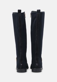 Bottes hautes bleu marine avec une texture côtelée, accents en daim et fermeture éclair à l'arrière. Semelles plates et détail de logo sur le talon.
