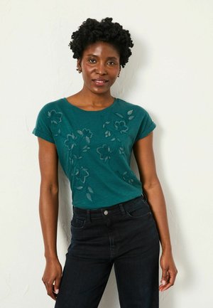 Teal short-sleeve t-shirt with floral embroidery on the front paired with dark high-waisted jeans. Smooth fabric, relaxed fit.