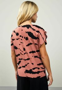 T-shirt à manches courtes en tissu rose avec un motif abstrait noir, présentant une coupe décontractée et une couture au dos pour plus de détail.