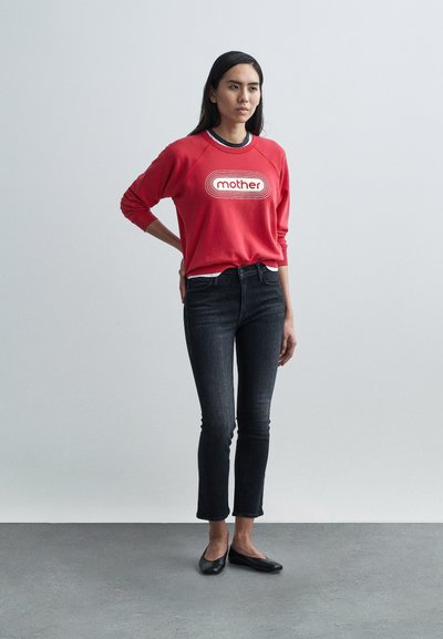 Raudonas džemperis su užrašu „mother“, juodos aptemptos džinsai ir juodi batai be aukštakulnių. Džempyje yra apvalus kaklo iškirpimas ir raglan rankovės.