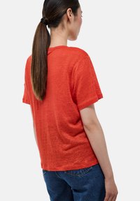 T-shirt rouge à manches courtes en tissu léger et texturé, avec une coupe décontractée, un col rond et des épaules légèrement tombées, associé à un jean.