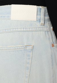Los jeans de mezclilla azul claro presentan una etiqueta de cuero con "CLOSED" en relieve. La tela tiene un aspecto desgastado con costuras visibles y un bolsillo trasero.