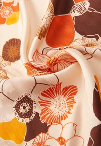 Tejido floral con un fondo beige que presenta flores en tonos naranja, marrón y amarillo. Textura suave con patrones detallados y colores vibrantes.