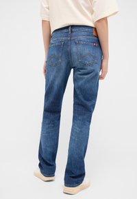 Siniset farkut suorilla lahkeilla, joissa on kaksi takataskua ja kontrastitikkaukset. Yhdistetty vaalean väriseen paitaan ja tennareihin.