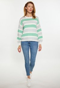 Suéter de punto a rayas en verde menta y gris, cuello redondo, mangas largas, combinado con jeans azules y zapatillas blancas. Textura suave, ajuste relajado.