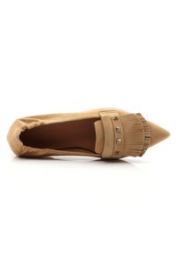 Scarpa piatta in suede beige con punta affusolata, frange decorative e borchie metalliche sulla fascia, dotata di un morbido elastico attorno all'apertura.