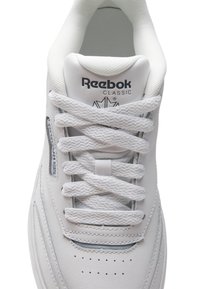 Baskets en cuir blanc avec bout rond, lacets plats et col rembourré. Présente un logo Reebok et de petites perforations sur la boîte à orteils.