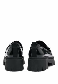 Mocassins à plateforme en cuir verni noir avec semelles épaisses rainurées et languettes au talon, vus de dos.