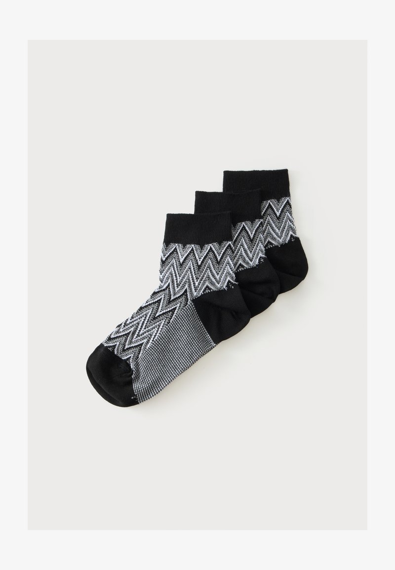 Trois paires de chaussettes noires et grises à cheville avec un motif en zigzag empilées sur un fond blanc.