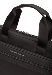 Μαύρη τσάντα φορητού υπολογιστή από νάιλον με επίπεδο σχεδιασμό, διπλά φερμουάρ και λογότυπο στο μπροστινό μέρος. Διαθέτει ανθεκτικές υφασμάτινες λαβές για εύκολο κράτημα.