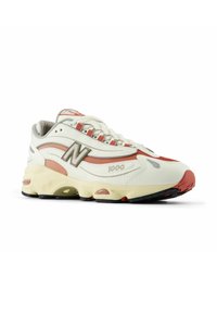 Weiße und korallenfarbene Sneaker mit Obermaterial aus strukturiertem Leder, gepolstertem Schaft und kontrastierender Gummisohle. Enthält "1000"-Label und Logo-Akzente.