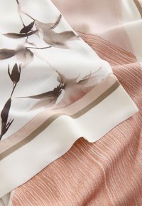 Mjukt tyg med ett blommönster i beige och bruna toner, draperat över texturerat rosa tyg med vita strimmor.