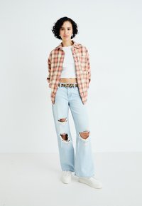 Skjorte med ruder i lys fersken og fløde, hvidt crop top, slidte lyseblå brede jeans, hvide sneakers og et mønstret bælte.