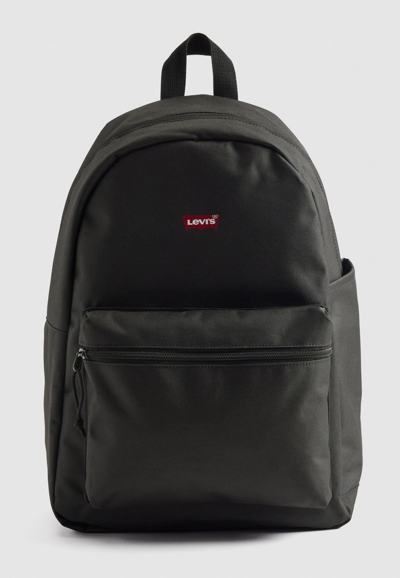 Mochila Levi's preta com bolso com fecho na frente e pega superior numa fundo claro e simples.