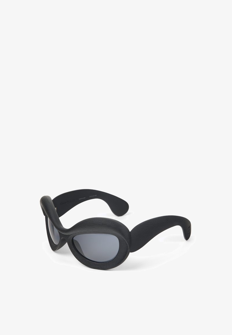 Černé sluneční brýle s hladkým, texturovaným povrchem. Oválné čočky a široké, zakřivené boční strany pro celkové pokrytí. Disponují elegantním, moderním designem.