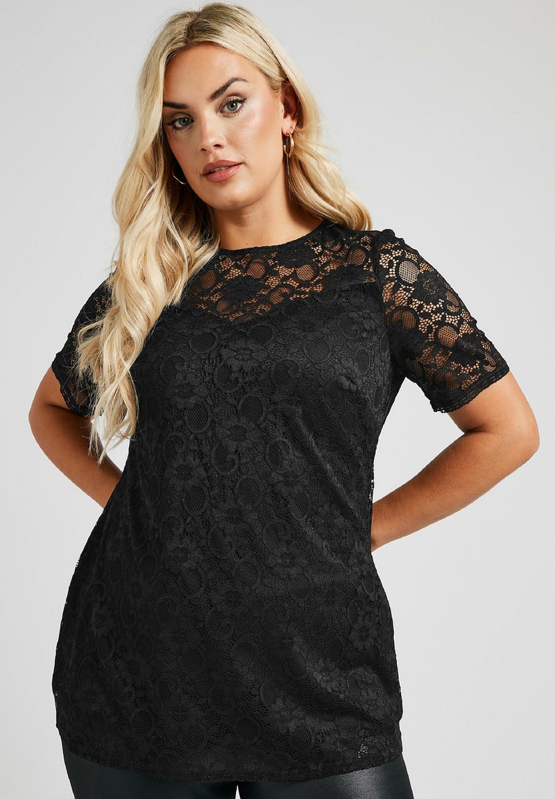 Top in pizzo nero con maniche corte e un motivo floreale, con un tessuto liscio sottostante. Design semi-trasparente con scollo rotondo.