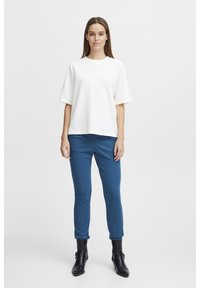 Vit kortärmad topp som kombineras med blå slim-fit-byxor och svarta anklarstövlar. Slät tyg med en avslappnad passform och enkel design.