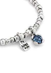 Pulsera de cuentas plateadas con un colgante de piedra preciosa azul y una etiqueta grabada con "UNO de 50" sobre un fondo blanco.