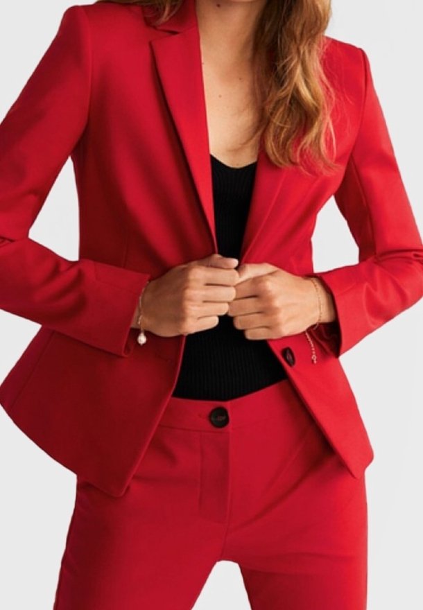 Blazer rouge ajusté associé à un pantalon coupe ajustée assorti, doté de revers en pointe, de fermeture à un bouton et d'une texture de tissu lisse.