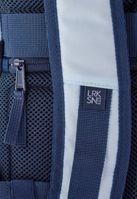 Rucsac de marin, evidențiind materiale din plasă și țesătură, detaliat cu curele reflectorizante și un mic eticheta care spune "LRK SN 2020." Buzunar cu fermoar vizibil.