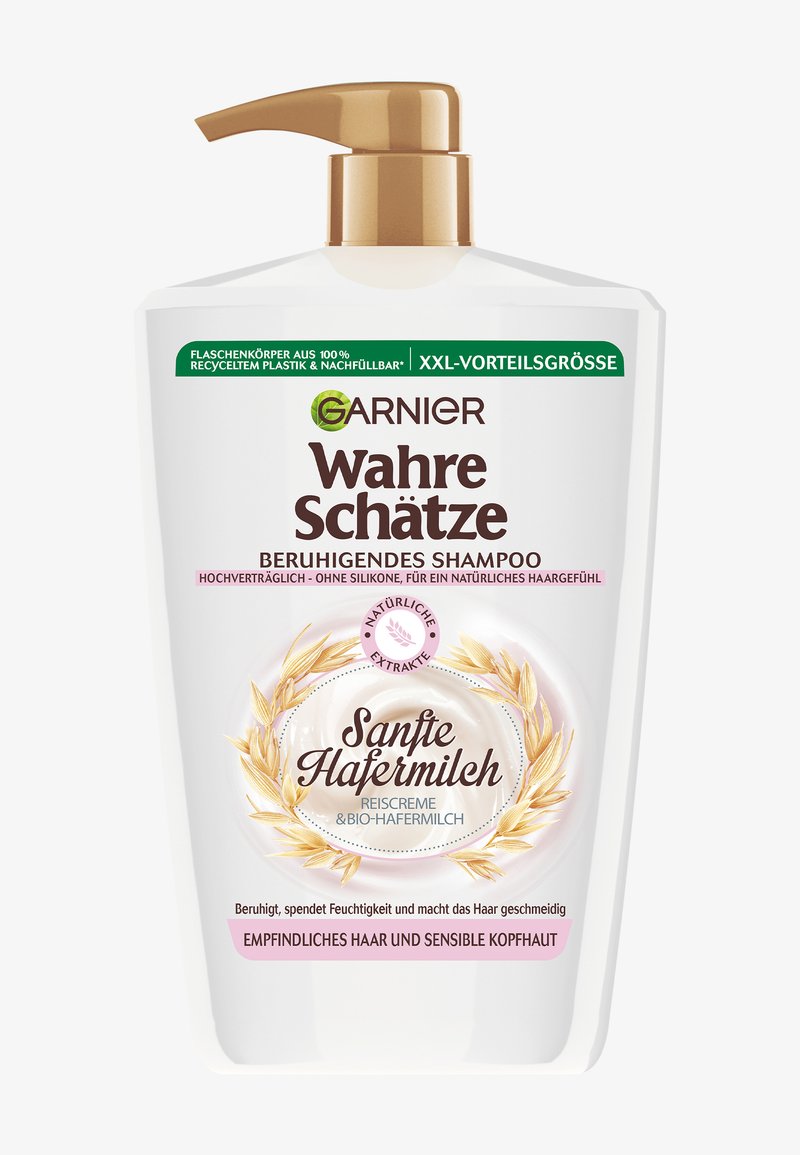 Biała butelka z pompką, oznaczona napisem "Garnier Wahre Schätze" dla kojącego szamponu. Posiada złote akcenty, kwiatowy wzór oraz informację o możliwości recyklingu.