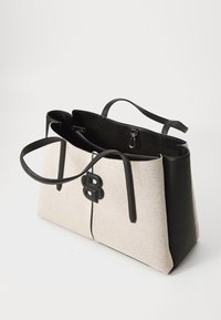 Beige lerret tote-bag med svarte skinn-detaljer og stropper. Har et fremtredende svart logo. Åpen topp med innerlommer for organisering.