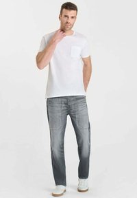 T-shirt blanche à manches courtes avec une poche poitrine, assortie à un pantalon en denim gris. L'ensemble est complété par des baskets blanches avec une semelle beige.