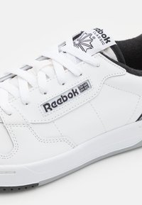 Vita lädersneakers med svarta accenter, Reebok-logotyp, rund tå, platt sula och texturerad snörningsdetalj. Klassisk design, minimalistisk stil.
