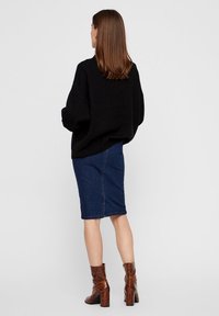 Oversized zwarte gebreide trui, midi-denimrok en bruine enkellaarsjes met slangenpatroon en blokhak. Zicht van achteren.