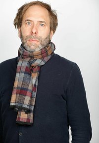 Karierteter Schal in Braun, Rot, Grau und Marineblau, aus weichem Stoff gefertigt. Um den Hals gewickelt über einem dunklen Pullover getragen.