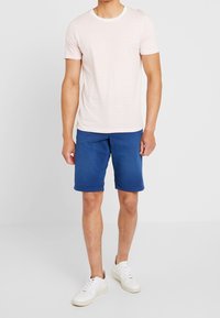 Vaaleanpunainen ja valkoinen raidallinen lyhythihainen t-paita yhdistettynä sinisiin shortsit ja valkoisiin lenkkareihin. Yksinkertainen muotoilu, rento istuvuus ja pehmeä kangas.