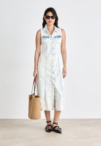 Ljusblå denimklänning utan ärmar med knappstängning fram, två bröstfickor och rak skärning. Vävda beige tote-väskan och svarta klacksandaler.