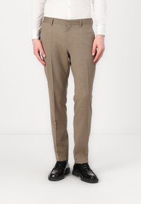 Pantaloni a quadri beige con vestibilità slim, tasche laterali e passanti per la cintura. Abbinati a scarpe in pelle nere, l'outfit ha un aspetto sartoriale.