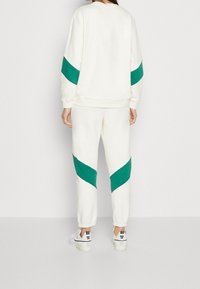 Felpa bianca e pantaloni della tuta con strisce diagonali turchesi, realizzati in materiale morbido. Abbinati a sneakers bianche con dettagli neri.