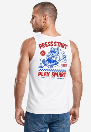 Man wearing white sleeveless shirt with red and blue graphic of a cat playing video games and text saying "Press Start Play Smart."