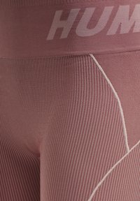 Rosa ribbade leggings har en bred midja med "HUM" text. Vit sömnad skapar ett geometriskt mönster längs sid sömmarna. Mjuk textur.