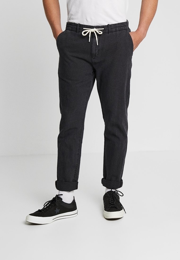 Zwarte taps toelopende broek met een elastische tailleband, opgerolde taille en bijpassende zwarte sneakers. De stof lijkt ademend en lichtgewicht te zijn.