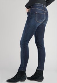Jeans skinny azul oscuro con cinco bolsillos, costuras en contraste y talle medio. Tela texturizada con ligero estiramiento para mayor comodidad.