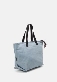 Ljusblå canvas toteväska med svarta handtag och dragkedjeaccenter. Stort rektangulärt format och texturerad yta. Enkel, funktionell design.