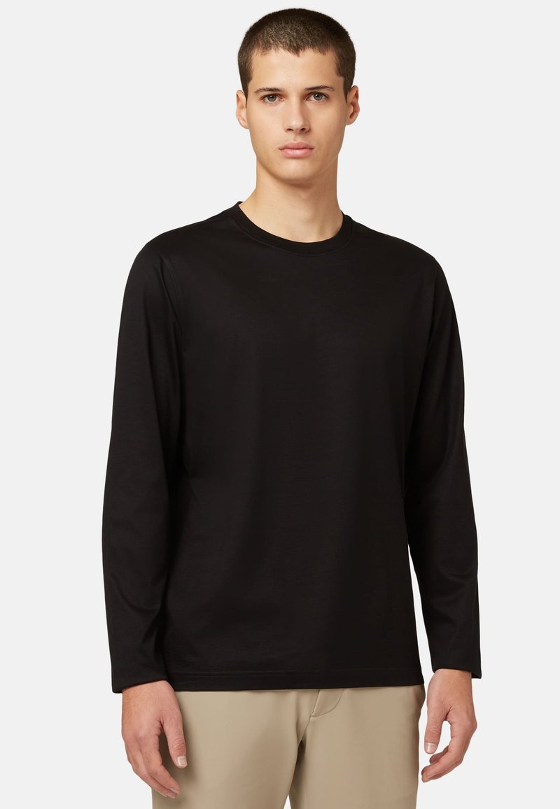 Must musta varrukatega särk siledast kangast, ümarate kaelustega, paremini istuva disainiga ja sirge lõikega, kantud beežide pükstega.